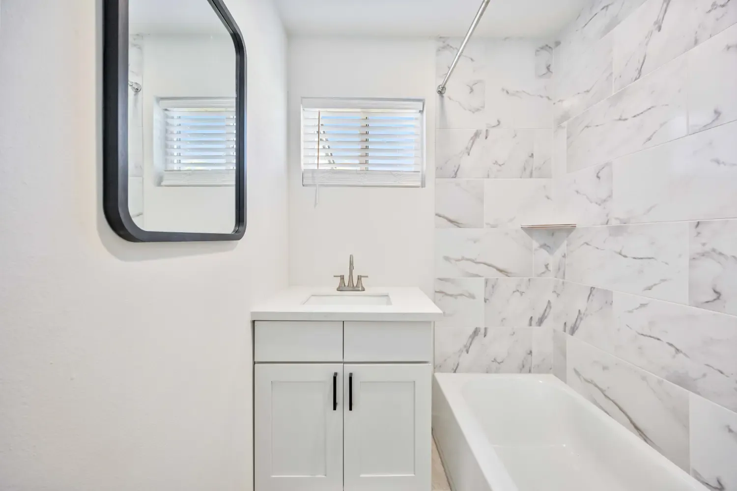 Bathroom with marble-look tile, tub and black-framed mirror